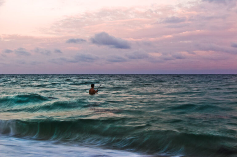 A long exposure photography image taken at sunset of a fisherman standing in the ocean