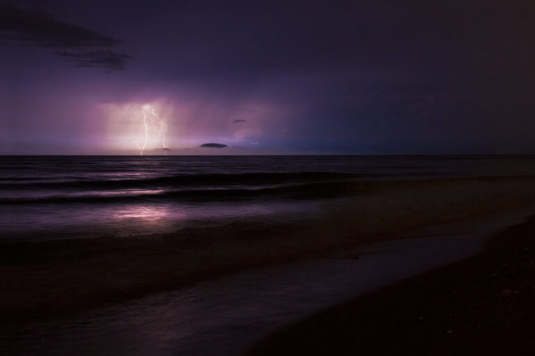 A long exposure photo of lightning striking the ocean at night