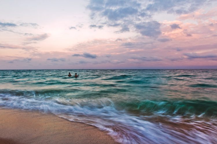 A long exposure of fishermen wading in the ocean at dusk