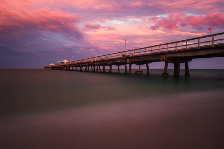 A long exposure seascape photo of a fishing pier at sunset