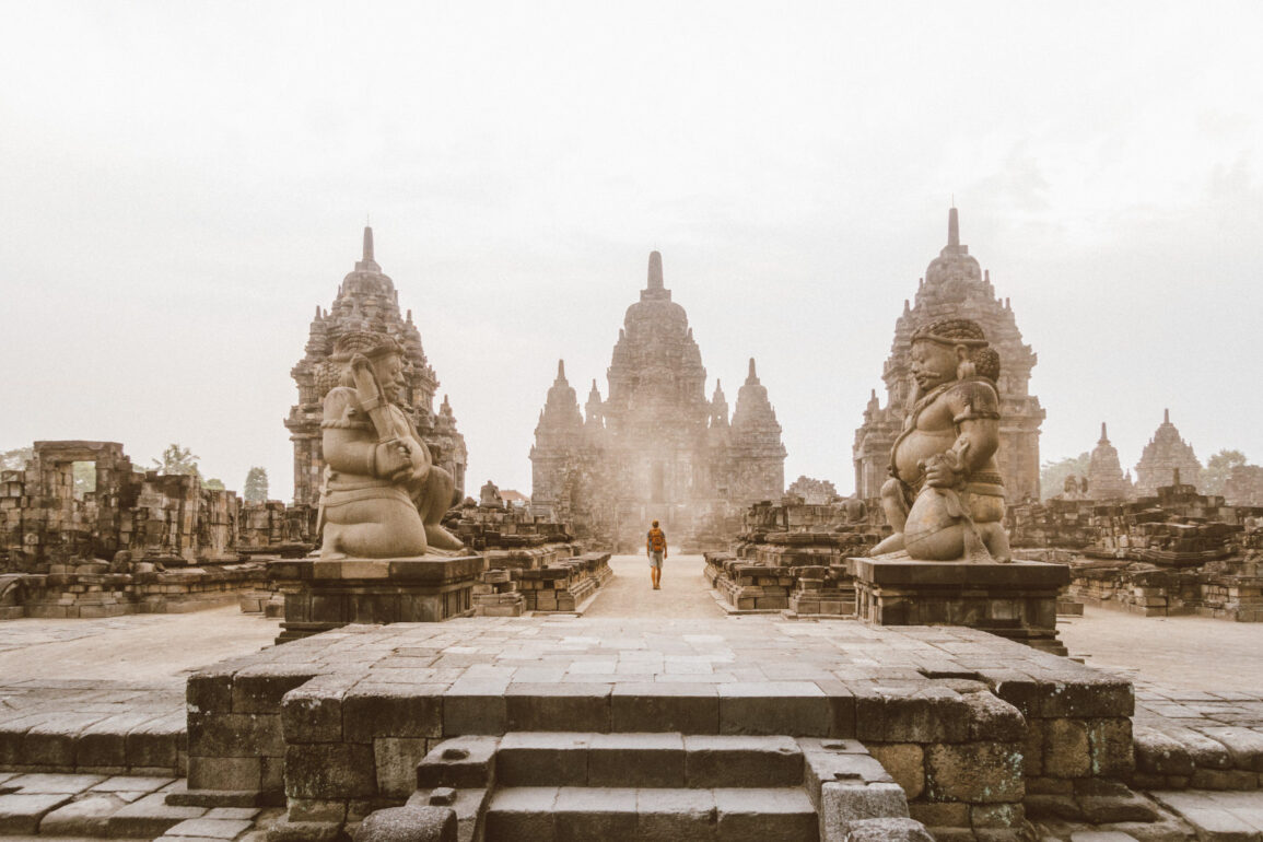 Traveler walking near an ancient temple in Indonesia, carrying a backpack and a Sawyer water bottle. Southeast Asia travel photography.