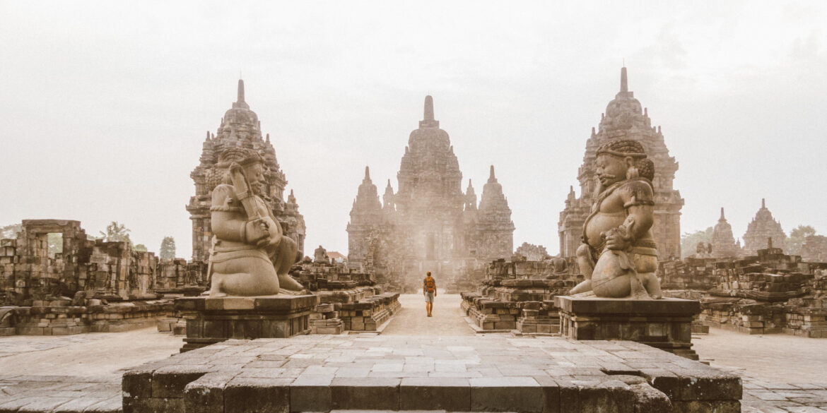 Traveler walking near an ancient temple in Indonesia, carrying a backpack and a Sawyer water bottle. Southeast Asia travel photography.