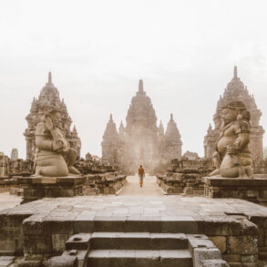 Traveler walking near an ancient temple in Indonesia, carrying a backpack and a Sawyer water bottle. Southeast Asia travel photography.