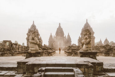 Traveler walking near an ancient temple in Indonesia, carrying a backpack and a Sawyer water bottle. Southeast Asia travel photography.